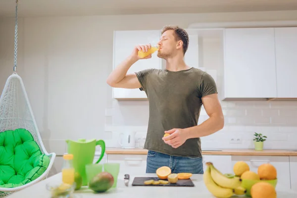 若いハンサムな男がキッチンで新鮮なオレンジ ジュースを飲みます。健康食品。菜食主義の食事。ダイエット デトックス — ストック写真