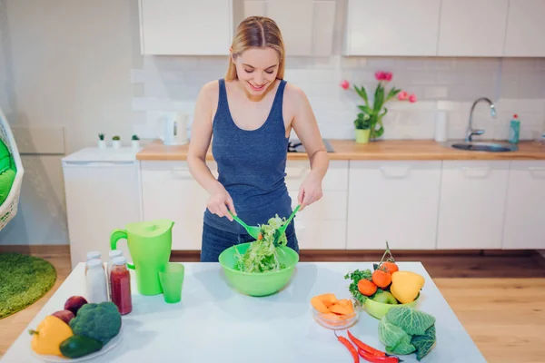 Vegan smiling blonde woman cooking delicious salad in the kitchen. Vegetarian food. Healthy eating. Vegan diet