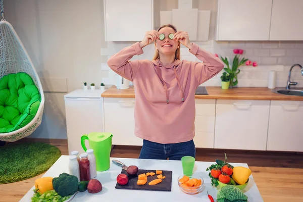 Vegán gyönyörű szőke nő is szórakoztató uborka, nyers zöldségek, a konyhában főzés közben. Nyers étrend. Vegetáriánus ételek. Egészséges táplálkozás — Stock Fotó