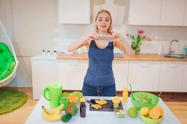 Mulher loira bonita Vegan com smartphone fotografar laranja orgânica na cozinha. Comida saudável. Desintoxicação da dieta — Fotografia de Stock