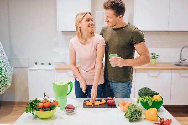 Vegan mutfak aile yemek çiğ sebze sevgi dolu. Genç kadın kesme sebze kocası ise sabah Detoks çay içer. Detoks diyet. Çiğ gıda diyet. Vejetaryen yiyecekler — Stok fotoğraf