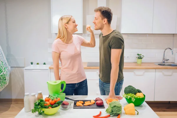 Jeune femme végétalienne donne morceau de légumes coupant son mari le matin. J'adore cuisiner des légumes bio en famille dans la cuisine. Désintoxication diététique. Alimentation crue. Alimentation végétarienne — Photo