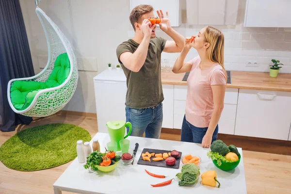 Jeune famille aimante s'amuse avec des tomates biologiques et du piment tout en cuisinant des légumes dans la cuisine blanche. Nourriture végétarienne. Joyeux couple. Aliments sains — Photo