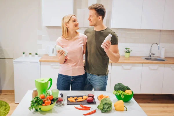 Vegan mutlu sevgi dolu çift beyaz mutfak çiğ sebze yemek yaparken şişe doğal yüzlü ile tutar. Detoks diyet. Mutlu bir aile. Çiğ gıda diyet. Vejetaryen yiyecekler. — Stok fotoğraf