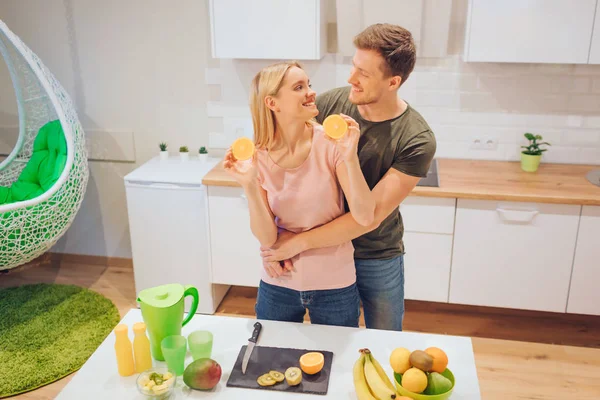 Jeune couple amoureux s'amuse avec orange biologique tout en cuisinant des fruits frais dans la cuisine blanche. Une nourriture saine. Bonne famille. Une alimentation saine — Photo