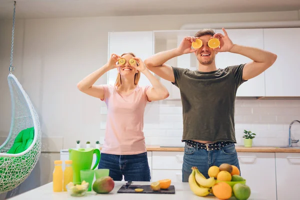 Jovem família amorosa se diverte com laranja orgânica enquanto cozinha frutas frescas na cozinha branca. Comida saudável. Um casal feliz. Alimentação saudável — Fotografia de Stock