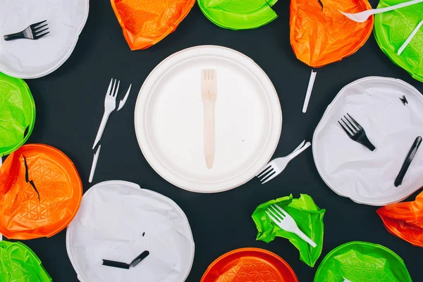 Sans plastique. Plaque et fourche en bois intactes au centre des plaques et fourches en plastique cassé jetables sur fond sombre, vue de dessus. Plastiques à usage unique, directive européenne en faveur de l'environnement — Photo