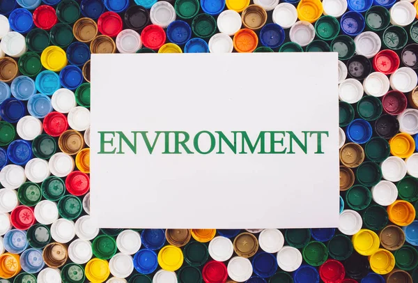 Plastic pollution concept. Be plastic free. Paper with word Environment on colored background of different plastic lids, top view. Single-use plastics, EU European directive to help environment — Stock Photo, Image