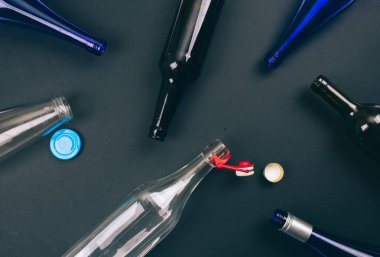 Yeniden geri dönüşümü azaltın. Boş renkli cam şişeler ve kapaklar karanlık arka planda geri dönüşüm için hazırlanır. Çevreyi koruyun. Üst görünüm