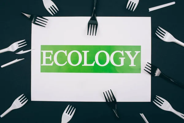 Be plastic free. Paper with word Ecology in the centre of single-use black and white plastic forks on dark background. Plastic is an evironmental problem. Refuse single-use plastic. Top view — Stock Photo, Image