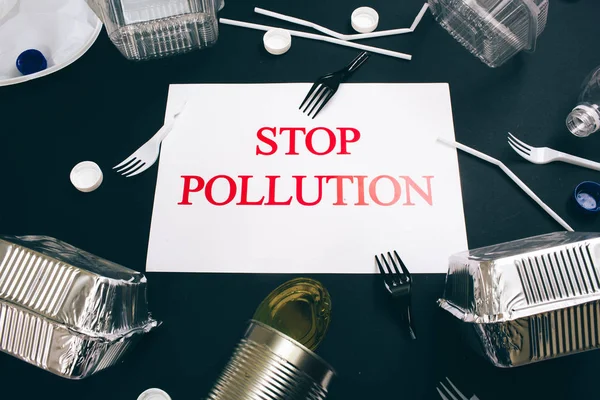 Plastic pollution concept. Paper with words Stop Pollution near single-use metal cans, foil containers, straws, broken forks, lids on dark background, top view. Single-use plastic. New rules to reduce — Stock Photo, Image
