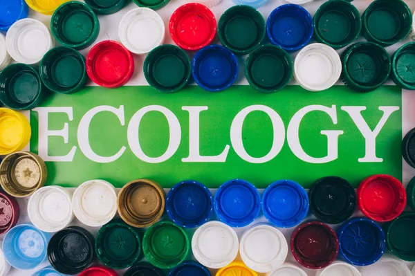 Recycling, reuse, reduce concept. Word Ecology in the center of colored background of different plastic lids, top view. Recycling bottle lids. Single-use plastics, EU European directive. Save ecology — Stock Photo, Image