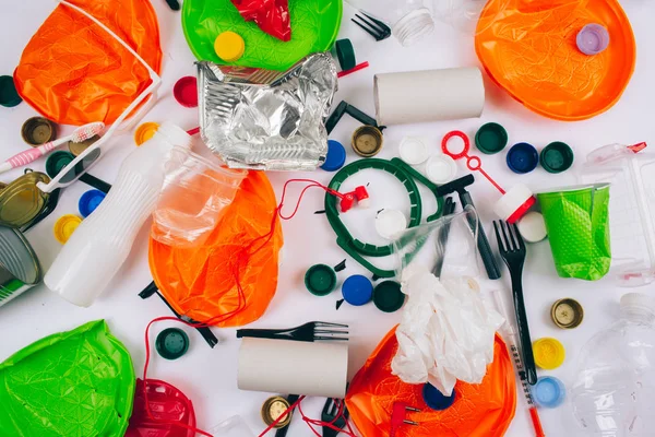 Plastic pollution concept. Be plastic free. Broken single-use colorful plates, forks, cups, bottle, straw, toothbrush, lids, foil and other plastic trash on white background. New rules to reduce