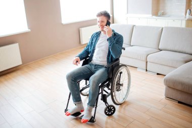 Engelli bir öğrenci tekerlekli sandalyede oturuyor ve telefonda konuşuyor. Boş odada tek başına. Kapsamı olan bir adam. Teknoloji ve modern aygıt.