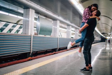 Young man and woman use underground. Couple in subway. Cheerful picture of young man holding woman in hands. She smile. Happy together. Love sotry. Underground modern urban view.