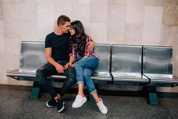 Młody mężczyzna i kobieta używają pod ziemią. Para w metrze. Siedzę na ławce. Pochylając się blisko siebie. Walentynki. Miłość od pierwszego wejrzenia. Miejski nowoczesny widok. — Zdjęcie stockowe