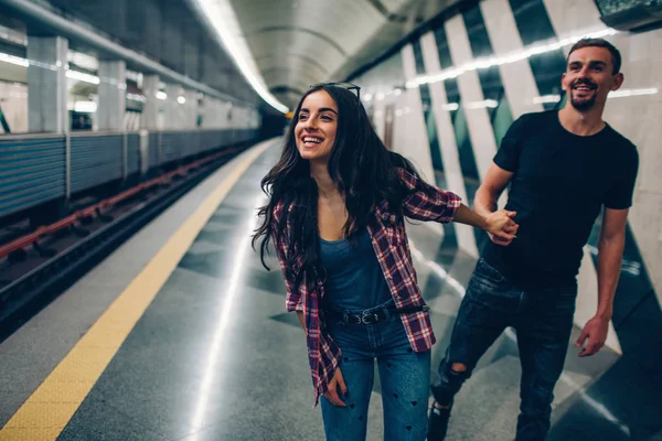 Mladý muž a žena používají podzemí. Pár v metru. Mladá žena drží muže v ruce. Sleduje ji. Mladá žena se usměje. Rychlý vlak jede. Akce. Milostný příběh. — Stock fotografie