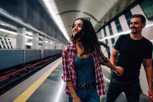 Mladý muž a žena používají podzemí. Pár v metru. Veselá fotka mladé ženy s mužem. Chytil ji za ruku a následoval modelku. Příběh lásky. Akce podzemí. — Stock fotografie