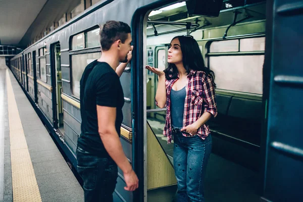Young man and woman use underground. Couple in subway. Lovely young woman send kisses to man. Guy look at her and smile. Together alone on platform and underground carriage. — Stock Photo, Image