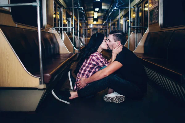 Jovem e mulher usam o subterrâneo. Um casal no metro. Adorável casal alegre sentar juntos no chão e beijando. Sozinho em carruagem subterrânea vazia. História de amor. Vista urbana moderna . — Fotografia de Stock