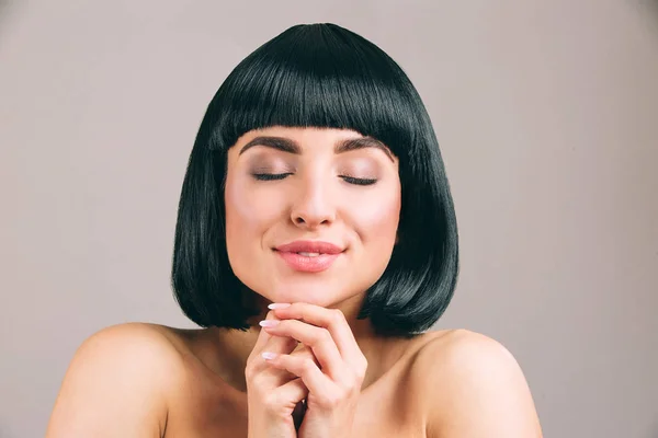 Jeune femme aux cheveux noirs posant à la caméra. Rêveur beau modèle garder les yeux fermés et les mains ensemble. Souris. Calme et paisible. Isolé sur fond clair . — Photo