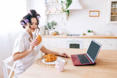 Genç kaygısız hizmetçi masaya otur ve kruvasan ye. Evden çalışıyorum. Laptop ve bir bardak içki masada. Mutfakta yalnızdım. Zengin baba her şeyi öder..