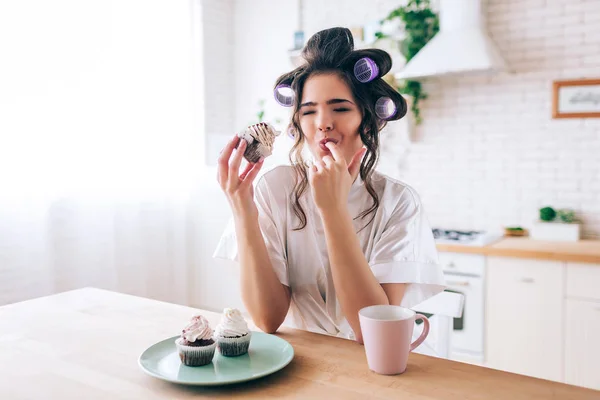 動揺不幸な若い女性は、上にクリームとパンケーキを食べます。指が漏れてるテーブルの上のカップとパンケーキ。キッチンで一人で朝の昼光. — ストック写真