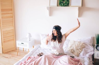 Koyu saçlı güzel genç esmer yatağında uyanmak. Germe ahnd ve esneme. Yatak odasında tek başına. Alnında uyku maskesi var. Sabah uyan..