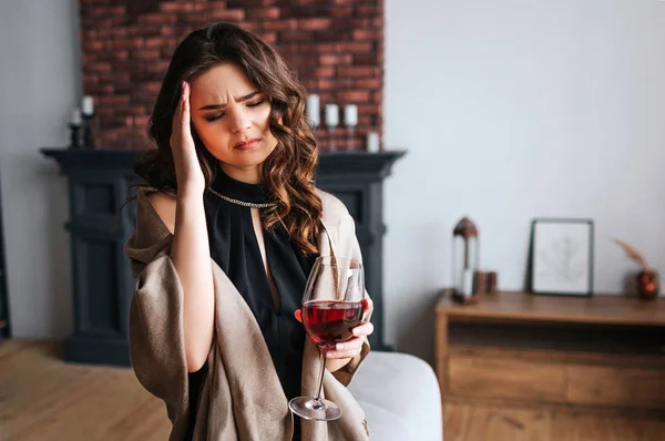 Die junge Geschäftsfrau arbeitet zu Hause. stehen im Wohnzimmer mit einem Glas Rotwein in der Hand. Kopfschmerzen. Allein. tragen schwarzes Kleid und braunes Tuch. — Stockfoto