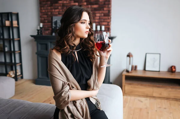 Ung affärskvinna arbetar hemma. Tankeväckande lugn modell håller glas rött vin och ser fram emot. Använd mörk klänning och brun tröja. Ensam i rummet. — Stockfoto