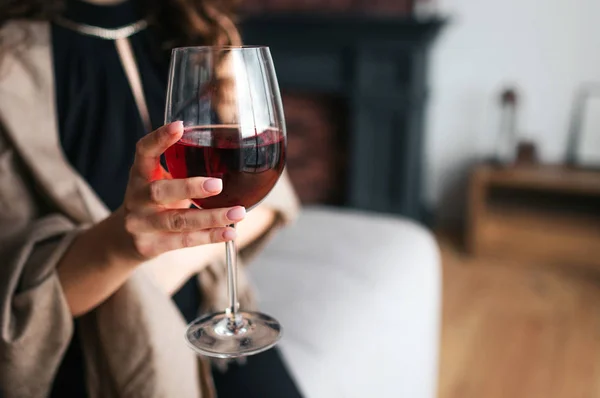 Cut vy av kvinnans hand hålla glas rött vin. Modell slitage svart klänning och brun sjal. Kvinna i vardagsrummet ensam. — Stockfoto