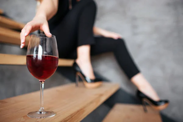 Ung kvinna har problem med alkohol. Cut vy av modellen når hand till glas med rött vin. Sitter bara på trappsteg. Snygg svart kvinnlig kostym. — Stockfoto
