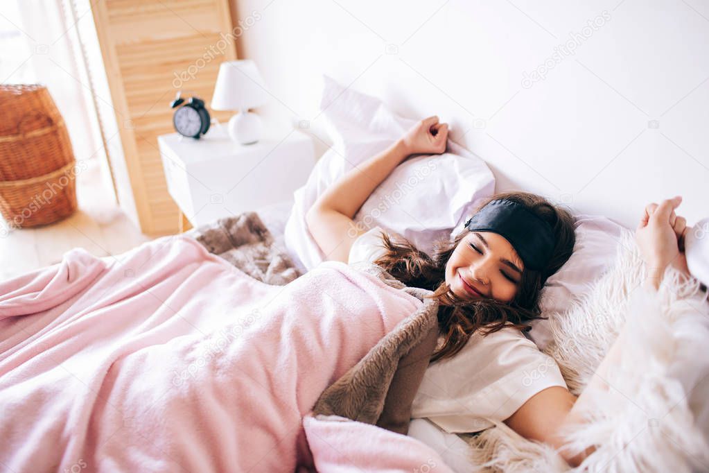 Dark haired beautiful young brunette wake up in her bed. Stretching hands and bosdy. Lying on bed in bedroom. Alone. Enjoying time in morning.