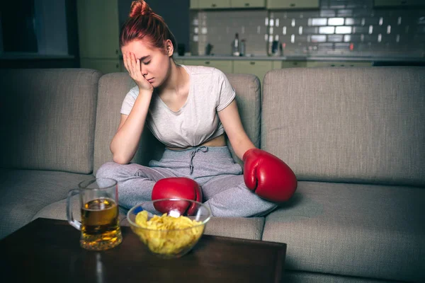 Mladá žena se v noci dívejte na box v televizi. Zmatený a nešťastný model se drží tváří v tvář. Sám na pokoji. Jink jídlo na stole. Temnoty. — Stock fotografie