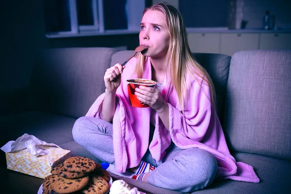 Jovem a ver filmes à noite. Modelo concentrado comendo sorvete com colher. Sentado no sofá no quarto sozinho. Programa de streaming ou série de tv . — Fotografia de Stock