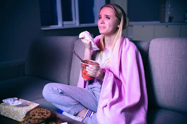 Девушка смотрит кино по ночам. Сидя на диване и плача. Смотрел печальное потоковое шоу или сериал. Есть мороженое и печенье . — стоковое фото