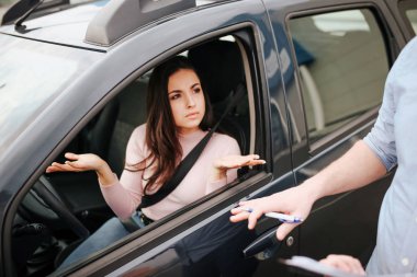 Male auto instructor takes exam in young woman. Disturbed confused model look out from car and wave with hands. Seat belt goes across body.