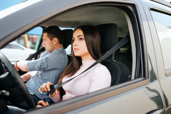 Homme instructeur auto prend examen chez la jeune femme. Brune sérieuse tenir la ceinture de sécurité dans la main et regarder droit. Guy se prépare pour la conduite . — Photo
