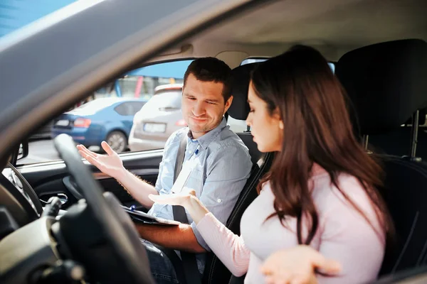Homme instructeur auto prend examen chez la jeune femme. Conflit en voiture. Les gens saluent avec les mains. Regardez dans la même direction. Asseyez-vous dans la voiture . — Photo