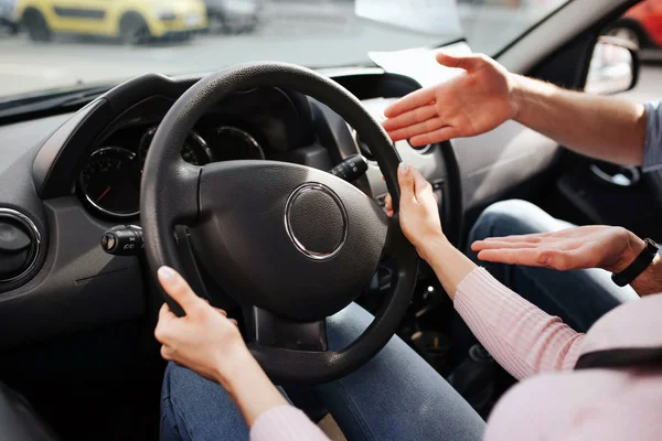 stock image Male auto instructor takes exam in young woman. Cut view of womans hands on steering wheel. Guy point on it and explain. Sit in car together. Exam time.