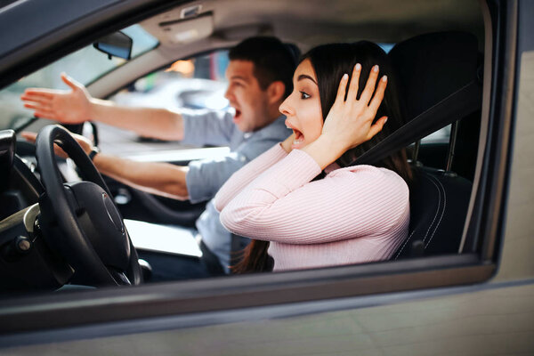 Male auto instructor takes exam in young woman. Screaming and yelling. Looking forward. Woman drive car but doesnt hold hands on steering wheel. Stress and discomfort.