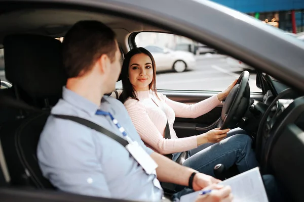 Male auto Instructor neemt examen in jonge vrouw. Rust vreedzame zelfverzekerde vrouwelijke student kijken naar leraar en glimlach. Houd de handen op het stuur en de aandrijving. — Stockfoto