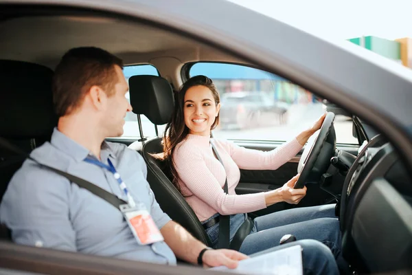 Mužská autoinstruktorka provádí zkoušku u mladé ženy. Veselý, atraktivní a pozitivní model se na člověka usmívá. S jistotou řídit vůz. — Stock fotografie