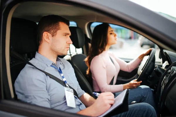 Male auto Instructor neemt examen in jonge vrouw. Zorgvuldige leraar kijkt vooruit. Student drive auto. Ernstige en geconcentreerde. — Stockfoto