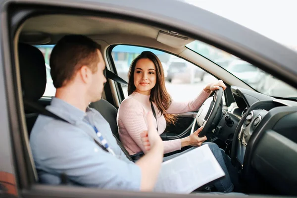 Instrutor automático masculino faz exame em mulher jovem. Modelo feliz positivo olhar para cara e sorrir. Dirigir carro sozinho e cuidadoso. O tipo fala com ela. Exame de aprovação . — Fotografia de Stock