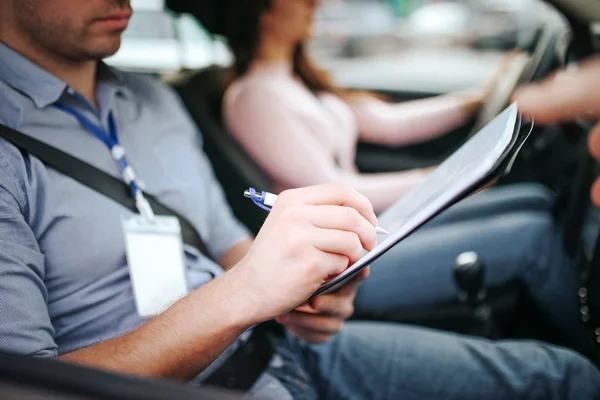 Hombre auto instructor toma examen en mujer joven. Primer plano del hombre escribiendo en papel. Pasando la prueba práctica. Mujer joven conduciendo con confianza . — Foto de Stock