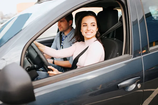 Hombre auto instructor toma examen en mujer joven. Joven alegre positiva y feliz conduciendo coche nd sonrisa. Instrucción sentarse además y examinarla . — Foto de Stock