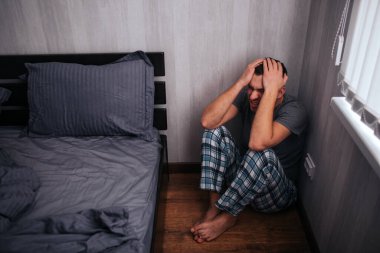 Depresyon, panik atak konsepti. Bir adam yatağın yanında bir köşede oturuyor. Kendini kötü hissediyor.