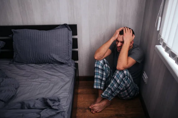 Depressionen, Panikattacken. Ein Mann sitzt in einer Ecke neben dem Bett. Er fühlt sich schlecht — Stockfoto