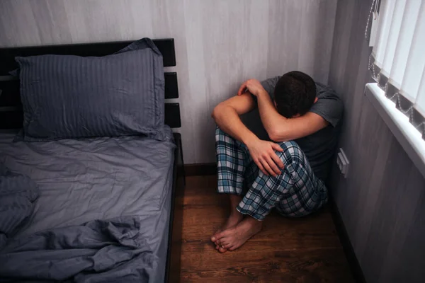 Depressão, conceito de ataque de pânico. Um homem está sentado num canto perto da cama. Ele sente-se mal — Fotografia de Stock